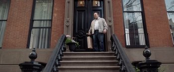 Movie still from “Hitch” (2005), directed by Andy Tennant – A man standing on the steps of a building holding a shopping bag; Wide shot, Low angle