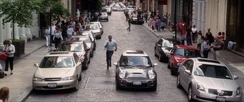 Movie still from “Hitch” (2005), directed by Andy Tennant – A man walking down a street past a line of parked cars; Wide shot, High angle
