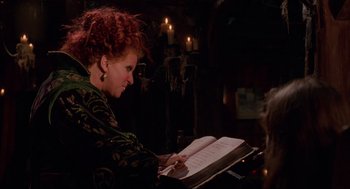 Movie still from “Hocus Pocus” (1993), directed by Kenny Ortega – A woman with red curly hair is reading a book; Medium shot, Over the shoulder angle