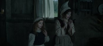 Movie still from “Hocus Pocus 2” (2022), directed by Anne Fletcher – Two young girls dressed in period clothing standing next to each other in front of a window; Medium shot, Low angle