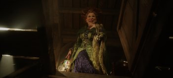 Movie still from “Hocus Pocus 2” (2022), directed by Anne Fletcher – A woman dressed as the witch is holding a bag; Medium shot, Low angle