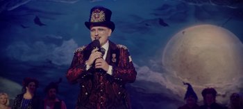 Movie still from “Hocus Pocus 2” (2022), directed by Anne Fletcher – A man wearing a top hat holding a microphone in his hand; Medium shot, Low angle