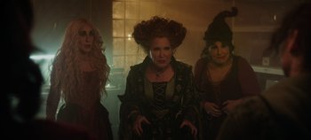 Movie still from “Hocus Pocus 2” (2022), directed by Anne Fletcher – A group of women standing next to each other in a dimly - lit room; Medium shot, High angle