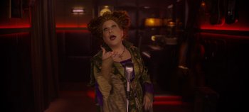 Movie still from “Hocus Pocus 2” (2022), directed by Anne Fletcher – A woman with red curly hair is singing into a microphone; Medium shot, Low angle