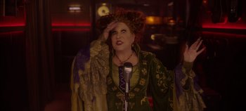 Movie still from “Hocus Pocus 2” (2022), directed by Anne Fletcher – A woman dressed as hocus pocus holding a microphone; Medium shot, Over the shoulder angle