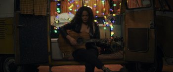 Movie still from “Holiday Harmony” (2022), directed by Shaun Paul Piccinino – A woman sitting on top of a bench playing a guitar; Medium shot, High angle