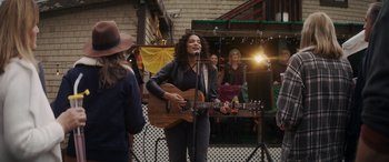 Movie still from “Holiday Harmony” (2022), directed by Shaun Paul Piccinino – A woman holding a guitar and singing into a microphone; Wide shot, Over the shoulder angle