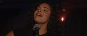 Movie still from “Holiday Harmony” (2022), directed by Shaun Paul Piccinino – A woman with curly hair is singing into a microphone; Close Up shot, Low angle
