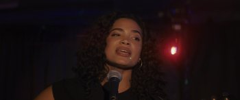 Movie still from “Holiday Harmony” (2022), directed by Shaun Paul Piccinino – A woman with curly hair is speaking into a microphone; Close Up shot, Low angle