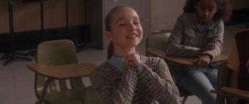 Movie still from “Holiday Harmony” (2022), directed by Shaun Paul Piccinino – A young girl sitting at a table with her hands under her chin; Medium shot, Over the shoulder angle