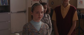 Movie still from “Holiday Harmony” (2022), directed by Shaun Paul Piccinino – A young girl with a headband is standing in front of other young girls; Close Up shot, Over the shoulder angle