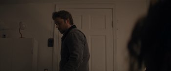 Movie still from “Holiday Harmony” (2022), directed by Shaun Paul Piccinino – A man standing in front of a white door; Medium shot, Low angle