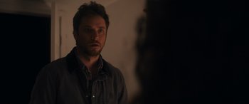 Movie still from “Holiday Harmony” (2022), directed by Shaun Paul Piccinino – A man standing in the dark looking at the camera; Close Up shot, Over the shoulder angle
