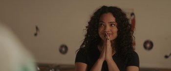 Movie still from “Holiday Harmony” (2022), directed by Shaun Paul Piccinino – A woman with curly hair is praying with her hands in the air; Close Up shot, Over the shoulder angle