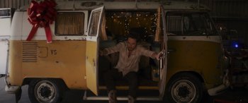 Movie still from “Holiday Harmony” (2022), directed by Shaun Paul Piccinino – A man sitting inside of an old yellow van; Wide shot, Low angle