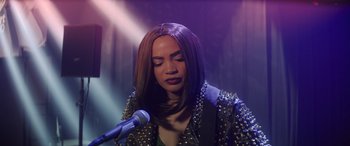 Movie still from “Holiday Harmony” (2022), directed by Shaun Paul Piccinino – A woman in a leather jacket holding a microphone in front of her face; Close Up shot, Over the shoulder angle