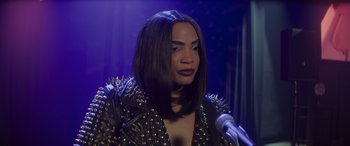 Movie still from “Holiday Harmony” (2022), directed by Shaun Paul Piccinino – A woman in a leather jacket is talking into a microphone; Close Up shot, Over the shoulder angle