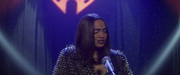 Movie still from “Holiday Harmony” (2022), directed by Shaun Paul Piccinino – A woman in a leather jacket is holding a microphone; Close Up shot, Over the shoulder angle