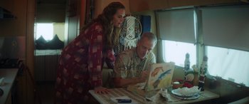 Movie still from “Holiday Harmony” (2022), directed by Shaun Paul Piccinino – A man and a woman looking at a painting on a table; Medium shot, Low angle