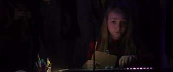 Movie still from “Holiday Harmony” (2022), directed by Shaun Paul Piccinino – A young girl sitting at a table writing on a piece of paper; Close Up shot, High angle