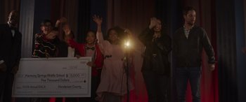 Movie still from “Holiday Harmony” (2022), directed by Shaun Paul Piccinino – A group of people standing on a stage with a microphone; Medium shot, Over the shoulder angle