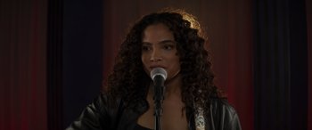 Movie still from “Holiday Harmony” (2022), directed by Shaun Paul Piccinino – A woman with long curly hair is speaking into a microphone; Close Up shot, Over the shoulder angle