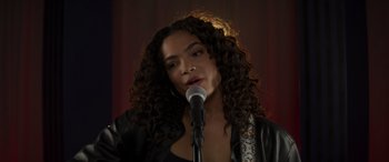 Movie still from “Holiday Harmony” (2022), directed by Shaun Paul Piccinino – A woman with curly hair is speaking into a microphone; Close Up shot, Over the shoulder angle