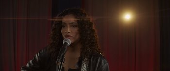 Movie still from “Holiday Harmony” (2022), directed by Shaun Paul Piccinino – A woman with curly hair is speaking into a microphone; Close Up shot, Over the shoulder angle