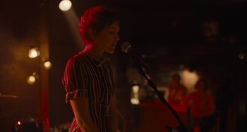 Movie still from “Hollywood Stargirl” (2022), directed by Julia Hart – A woman standing in front of a microphone on a stage; Medium shot, Over the shoulder angle