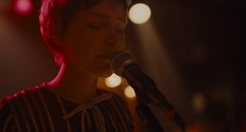Movie still from “Hollywood Stargirl” (2022), directed by Julia Hart – A woman is singing into a microphone in front of a crowd; Close Up shot, Low angle