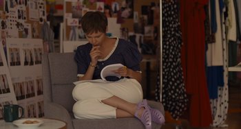 Movie still from “Hollywood Stargirl” (2022), directed by Julia Hart – A woman sitting on a couch holding a book; Medium shot, High angle