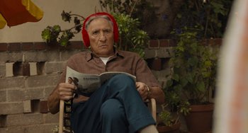 Movie still from “Hollywood Stargirl” (2022), directed by Julia Hart – An older man wearing red headphones while sitting in a chair; Close Up shot, Low angle