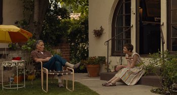 Movie still from “Hollywood Stargirl” (2022), directed by Julia Hart – Two people sitting on a porch with a potted plant in front of them; Wide shot, Over the shoulder angle