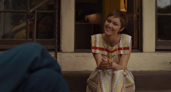 Movie still from “Hollywood Stargirl” (2022), directed by Julia Hart – A young woman in a colorful dress smiles while holding her hands out; Medium shot, Over the shoulder angle