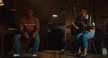 Movie still from “Hollywood Stargirl” (2022), directed by Julia Hart – A man and a woman sitting in front of an electric guitar; Medium shot, Over the shoulder angle