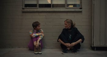 Movie still from “Hollywood Stargirl” (2022), directed by Julia Hart – A woman and a boy sitting next to each other on the sidewalk; Wide shot, High angle