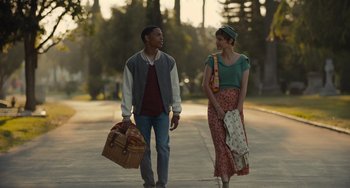 Movie still from “Hollywood Stargirl” (2022), directed by Julia Hart – A man and a woman walking down a street holding picnic baskets; Medium shot, Over the shoulder angle