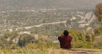 Movie still from “Hollywood Stargirl” (2022), directed by Julia Hart – A man sitting on top of a hill looking at a city; Extreme Wide shot, High angle