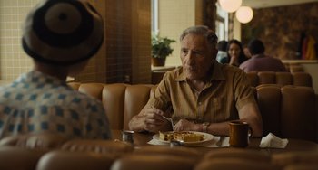 Movie still from “Hollywood Stargirl” (2022), directed by Julia Hart – An older man sitting at a table with a plate of food in front of him; Medium shot, Over the shoulder angle