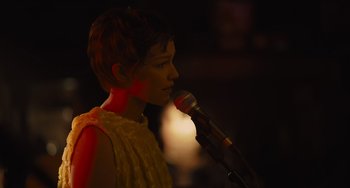 Movie still from “Hollywood Stargirl” (2022), directed by Julia Hart – A woman standing in front of a microphone in a dark room; Close Up shot, Over the shoulder angle
