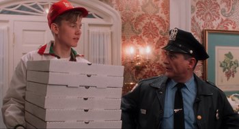 Movie still from “Home Alone” (1990), directed by Chris Columbus – A man and a boy are standing next to each other holding pizza boxes; Medium shot, Over the shoulder angle