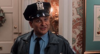 Movie still from “Home Alone” (1990), directed by Chris Columbus – A police officer wearing a leather jacket and a police hat; Medium shot, Low angle