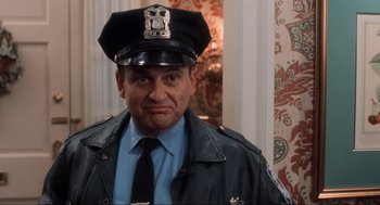 Movie still from “Home Alone” (1990), directed by Chris Columbus – A police officer in a leather jacket and a police hat; Medium shot, Low angle