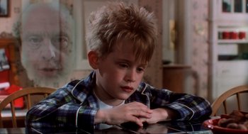 Movie still from “Home Alone” (1990), directed by Chris Columbus – A young boy sitting at a table with his hands folded over his face; Close Up shot, Over the shoulder angle