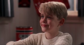 Movie still from “Home Alone” (1990), directed by Chris Columbus – A young boy with blonde hair and blue eyes smiling; Close Up shot, Low angle