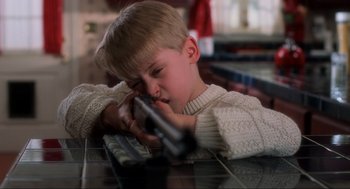 Movie still from “Home Alone” (1990), directed by Chris Columbus – A young boy is holding a gun in his hand; Extreme Close Up shot, Low angle