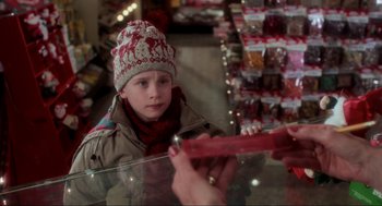 Movie still from “Home Alone” (1990), directed by Chris Columbus – A young boy in a hat is looking at a candy bar; Close Up shot, Over the shoulder angle