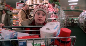 Movie still from “Home Alone” (1990), directed by Chris Columbus – A young boy in a shopping cart with a toilet paper roll in the cart; Close Up shot, Low angle
