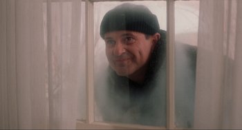 Movie still from “Home Alone” (1990), directed by Chris Columbus – A man in a black hat looking out a window; Medium shot, Low angle