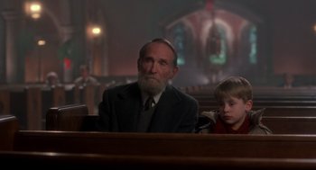 Movie still from “Home Alone” (1990), directed by Chris Columbus – An older man and a young boy sitting in a church; Medium shot, Low angle
